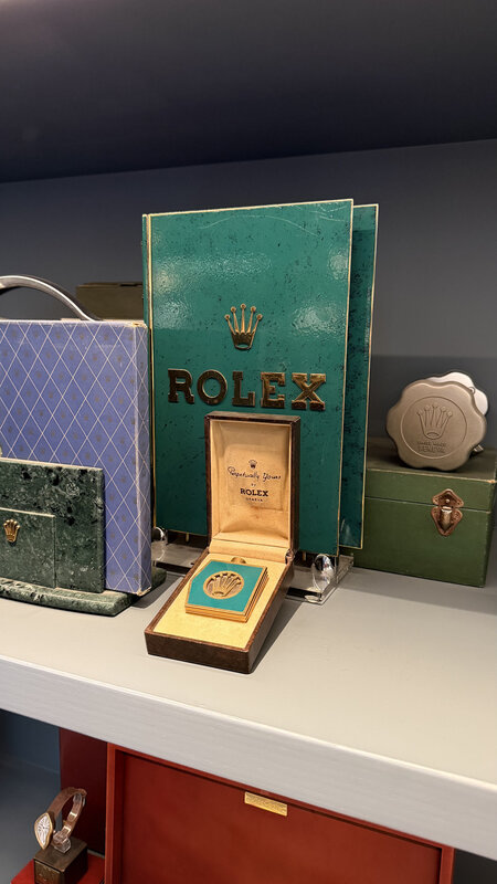 Green vintage Rolex presentation box opened on a shelf between older Rolex boxes and accessories
