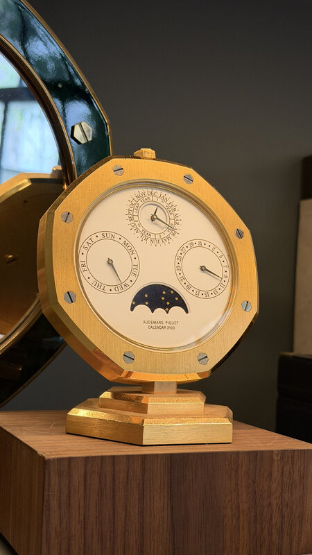 Gold Audemars Piguet Calendar 2100 octagonal desk clock with moonphase and triple calendar subdials, displayed on a wooden plinth
