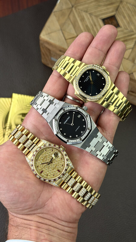 Three luxury watches held together in one hand — a gold diamond-bezel Patek Philippe, a steel diamond-bezel Audemars Piguet Royal Oak, and a gold pavé-diamond Rolex Day-Date with coloured stone markers