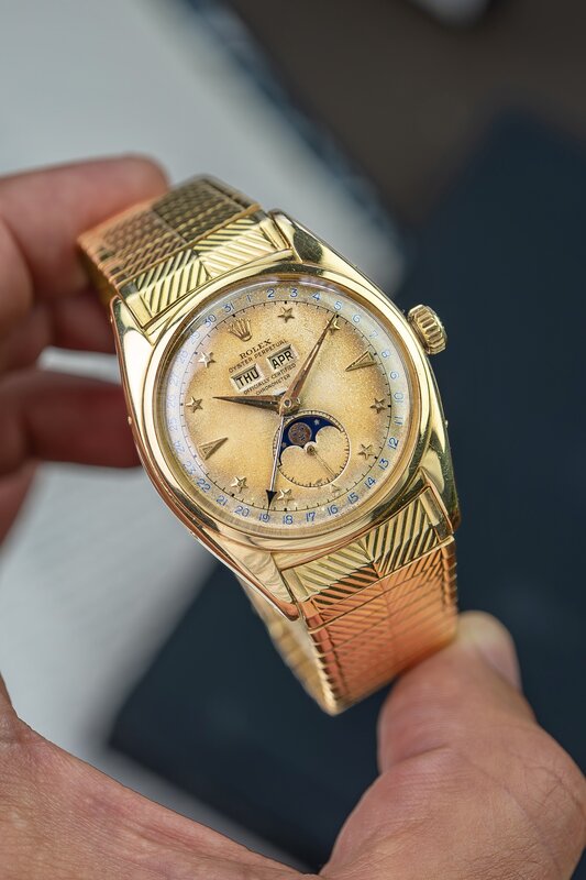 Vintage gold Rolex ref. 6062 Stelline moonphase triple calendar with star hour markers, day and month apertures, and an engraved gold bracelet, held up in one hand