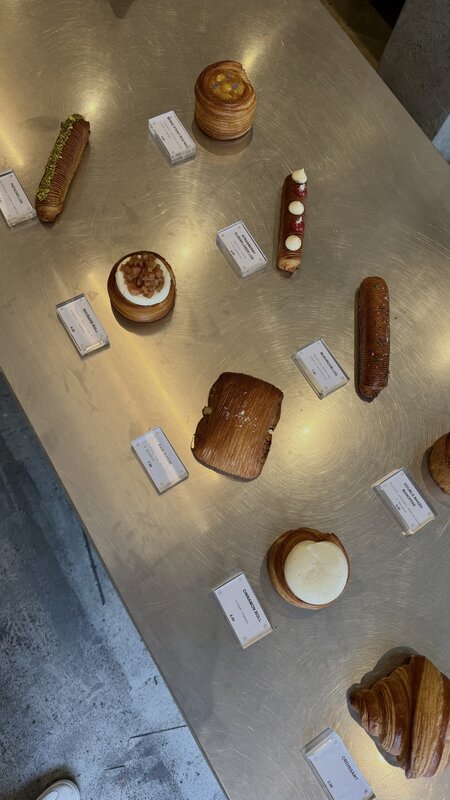 Pastries laid out on a brushed steel counter at Layers bakery in Amsterdam, each beside a small printed price card