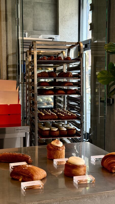 Interior of Layers bakery in Amsterdam, a tall rack of croissants and pastries behind the steel counter