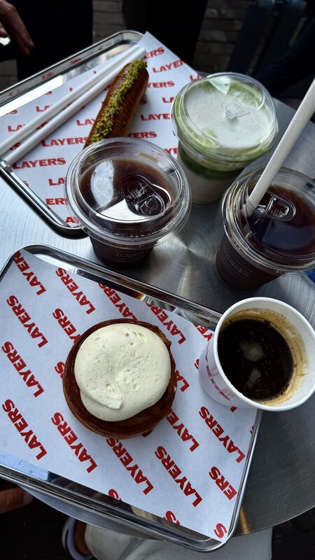 A Layers tray with a cream-topped cruffin, a pistachio eclair, iced coffees and a matcha, on branded red and white paper