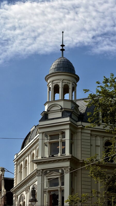 An ornate Amsterdam building with a domed corner cupola and spire against a blue summer sky