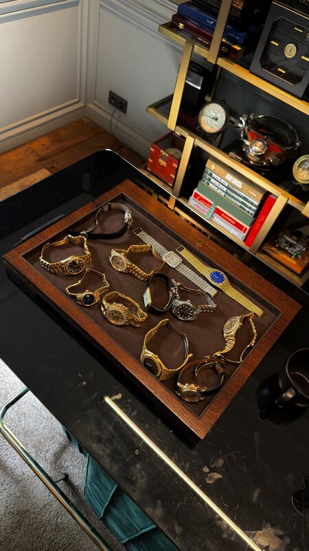 A wooden display tray of vintage gold watches at Amsterdam Vintage Watches, shelves of watch books and clocks behind it