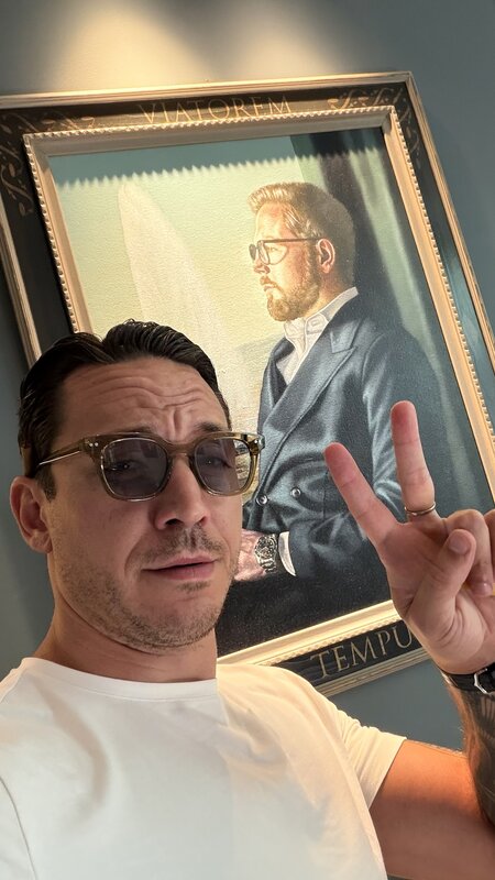 Jimmy in sunglasses holding up a peace sign in front of a framed painted portrait at Amsterdam Vintage Watches