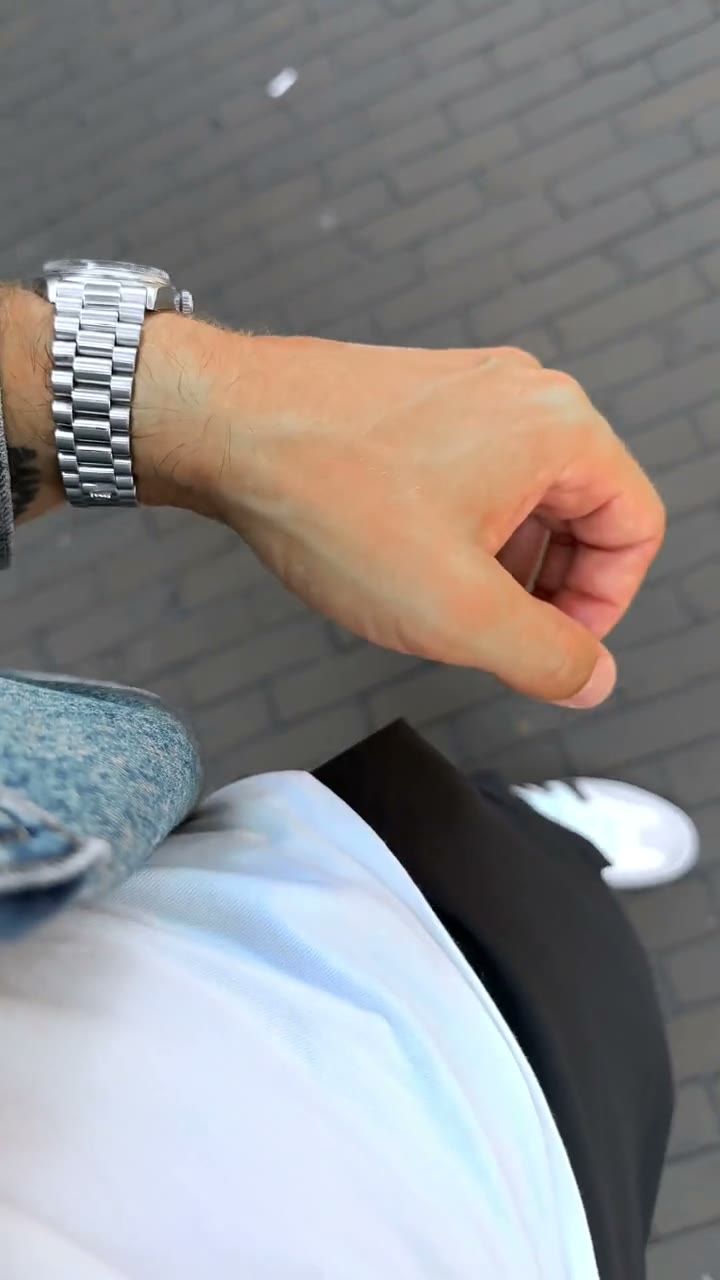 A steel Rolex Day-Date on a President bracelet worn on the wrist, walking over cobbles