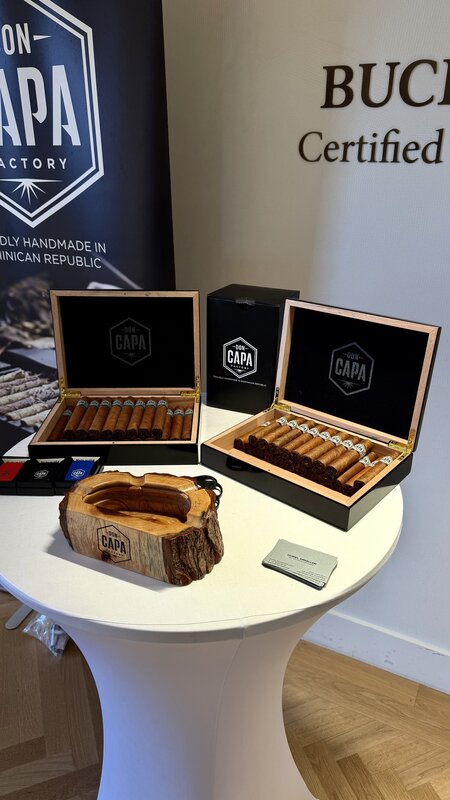 Open Don Capa cigar boxes arranged on a draped cocktail table beside a banner reading proudly handmade in the Dominican Republic, a Bucherer Certified banner behind