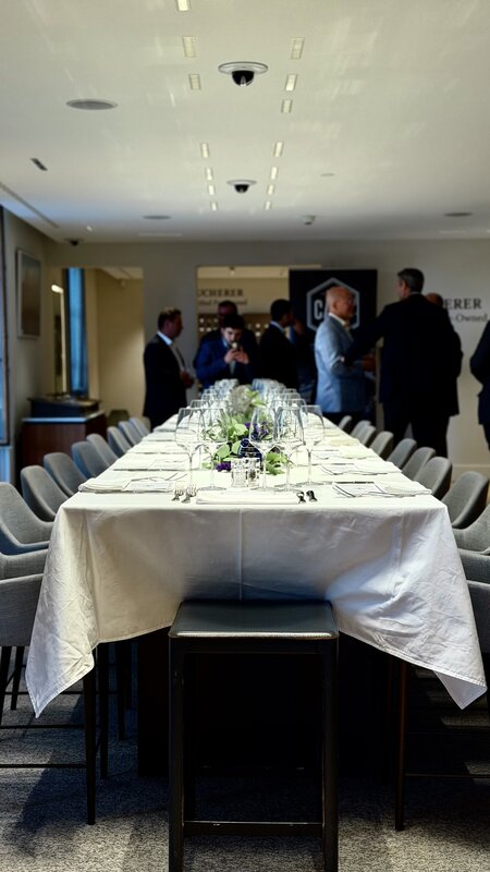 The dinner table seen down its length before service, guests standing and talking at the far end of the room