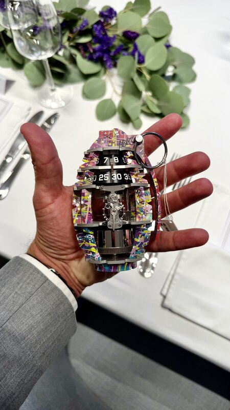 A multicoloured, grenade-shaped L'Epée 1839 table clock with two numbered drums, held in an open palm above the dinner table