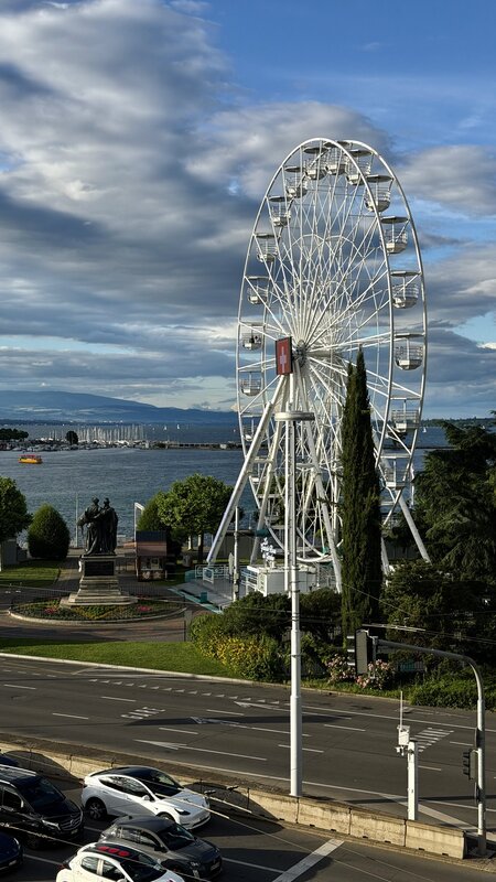 A Ferris wheel on Geneva's lakefront seen from above, with traffic and Lake Geneva behind it