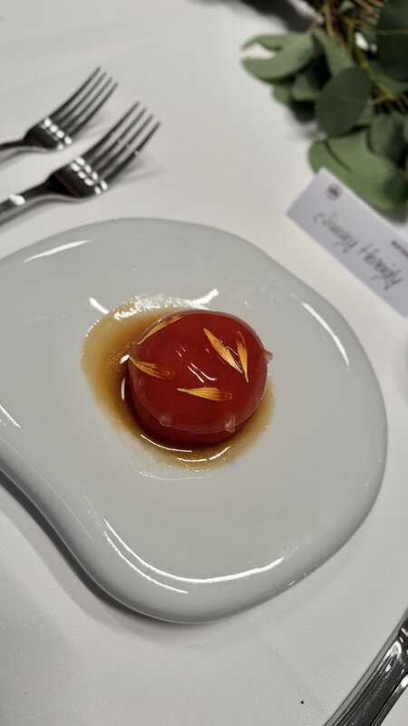 The tomato starter, a glossy red sphere in a shallow pool of sauce on a white plate