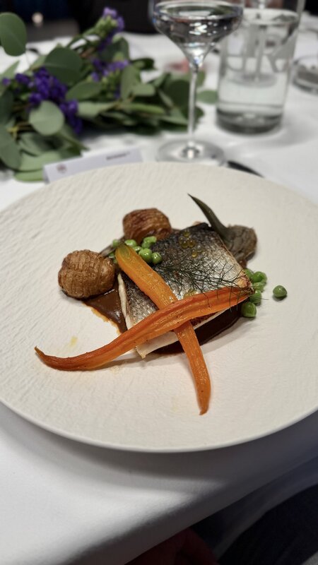 A sea bass fillet served with carrots, peas and small potatoes on a white plate