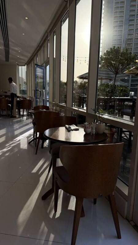 Empty restaurant table by floor-to-ceiling windows in Dubai — soft afternoon light, skyline outside