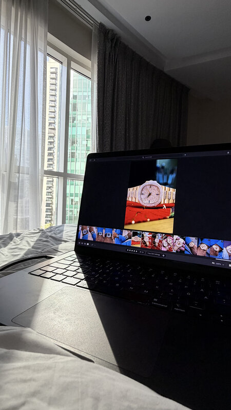 MacBook on a hotel desk in Dubai — image-editing software open with a gold watch on screen, curtains drawn