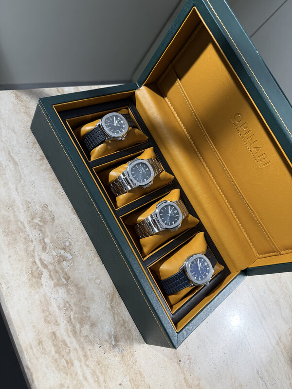 Four silver and steel watches arranged in an orange-lined display case on travertine — Collectors Gallery presentation