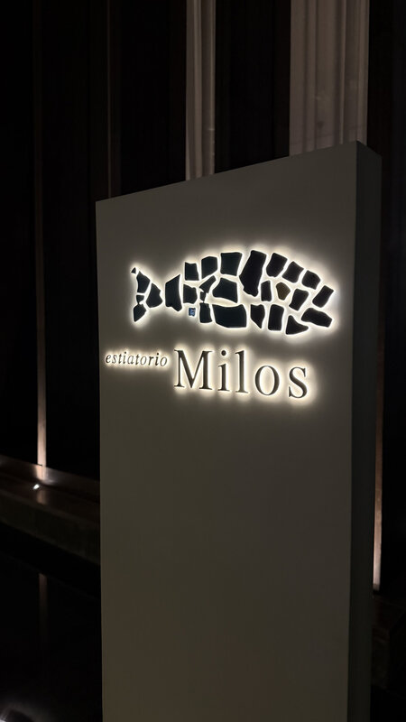 Estiatorio Milos signage outside the restaurant entrance at Atlantis the Palm — fish-shaped logo on a backlit white panel