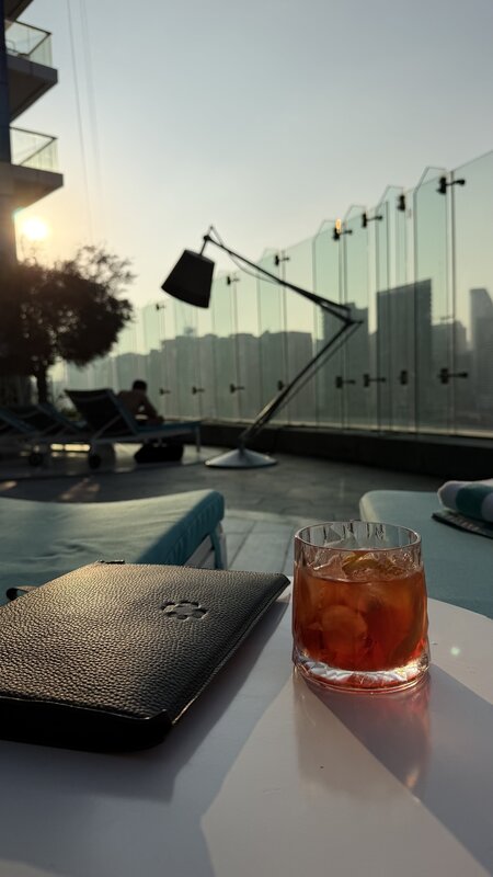 Cocktail glass and case on a white table at the Paramount pool — Dubai skyline behind at sunset