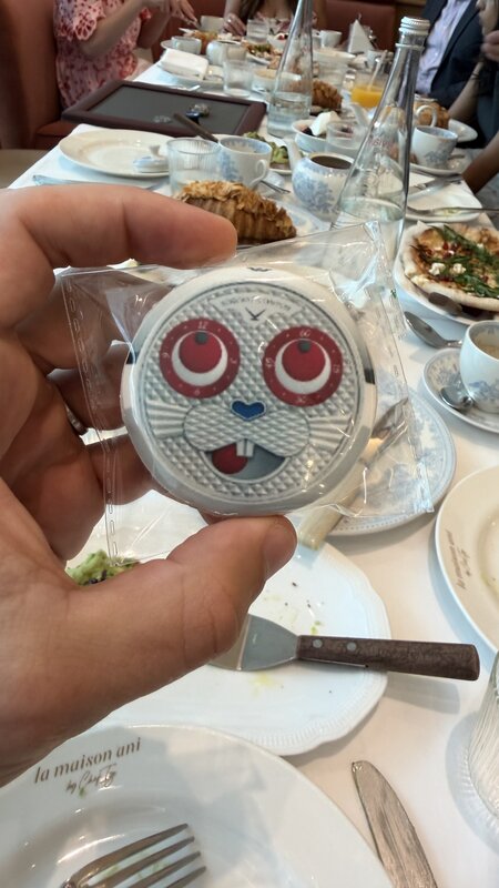 Konstantin Chaykin 'Rabbit' watch held above a restaurant table — round face, red eye markers, tongue dial