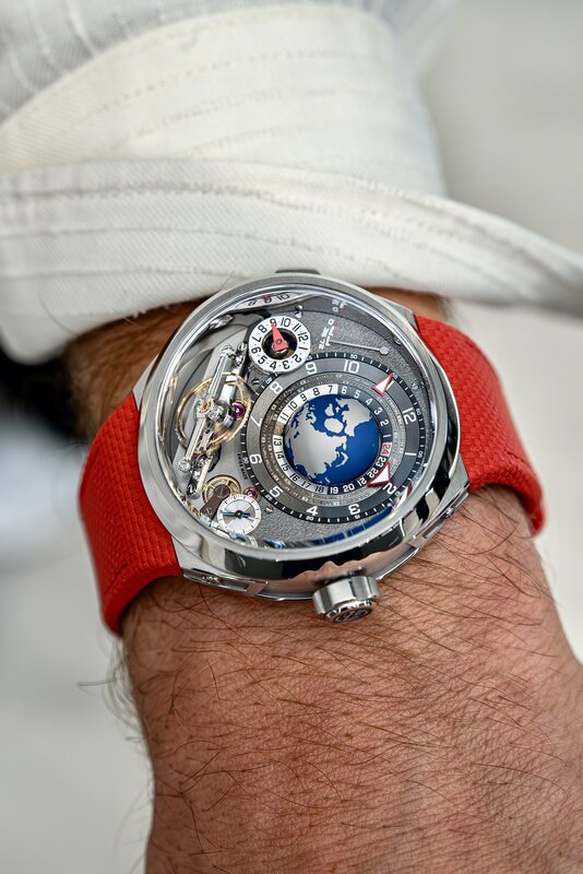Independent watchmaker world-time piece on wrist with red rubber strap — globe-style dial with red markers