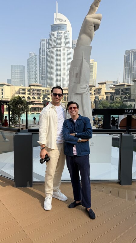 Jimmy standing with a fellow watch creator in front of the sculptural pointing-hand statue near Burj Khalifa — Dubai skyline behind