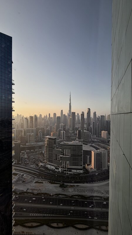 Dubai cityscape at sunset from a Paramount hotel window — Burj Khalifa and Business Bay towers, the highway below
