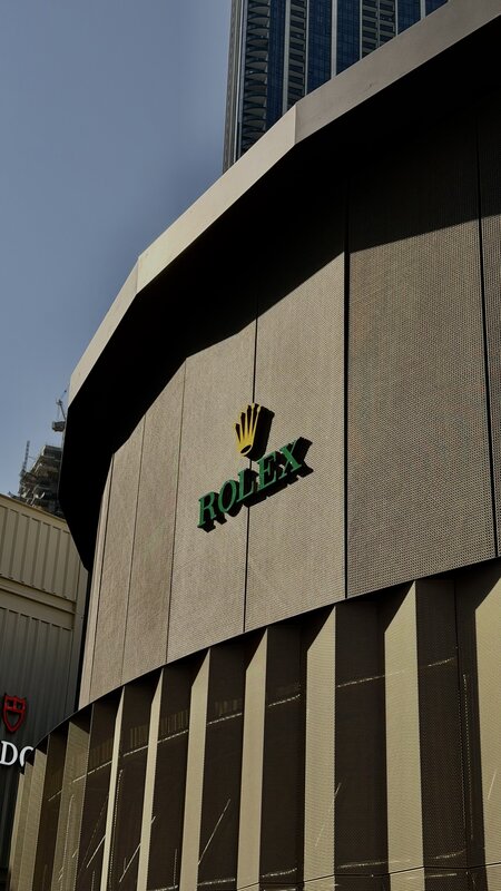 Curved Rolex boutique exterior at Dubai Watch Week — green Rolex crown logo on a warm-toned stone wall