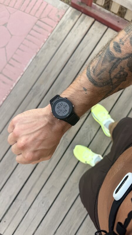 A Garmin watch reading 15.25 km on wooden decking, neon shoes below