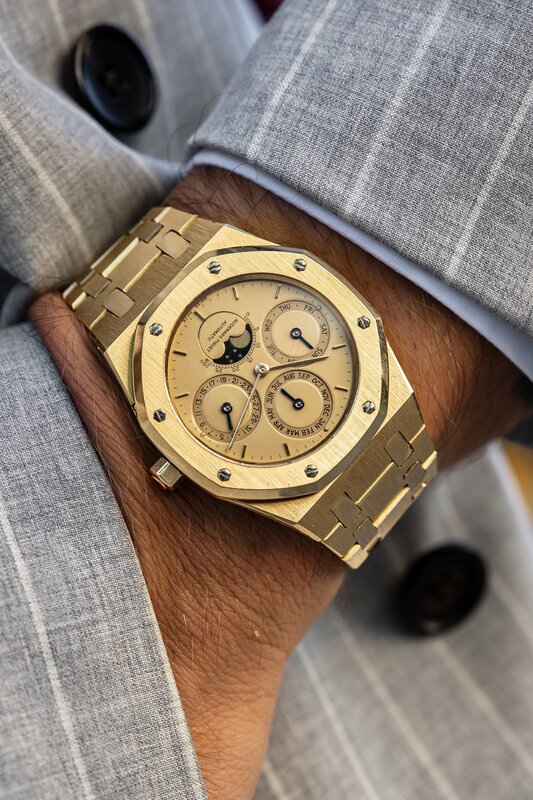 Yellow-gold Audemars Piguet Royal Oak perpetual calendar with a gold dial and integrated bracelet, worn under a grey pinstripe suit cuff