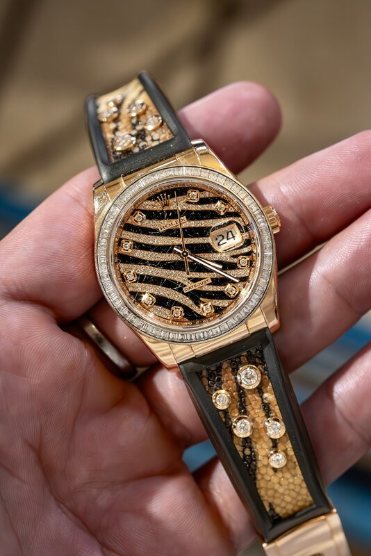 A gem-set Rolex Datejust with a tiger-stripe dial, baguette-set bezel and matching stone-set strap, held in one hand