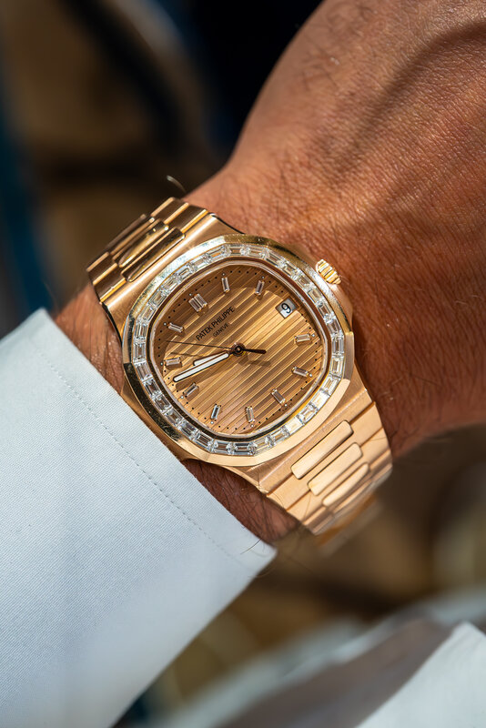 A yellow-gold Patek Philippe Nautilus with a diamond-set bezel and hour markers and an embossed gold dial on its integrated bracelet, under a white shirt cuff