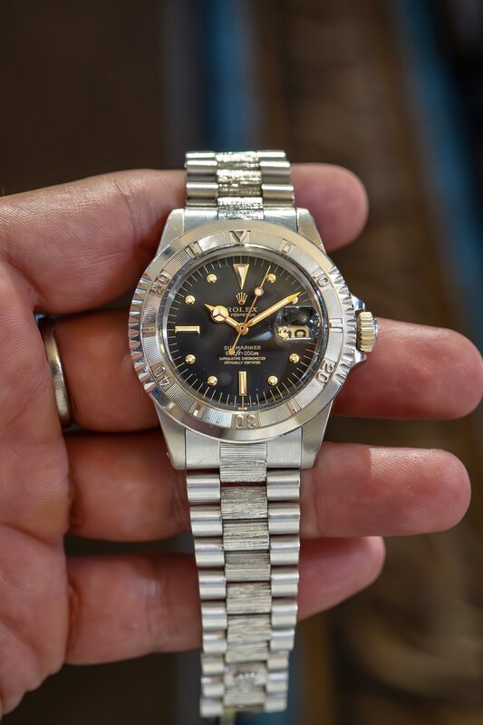 A vintage Rolex with a black Submariner dial, fluted bezel and a President-style bracelet, held in a hand