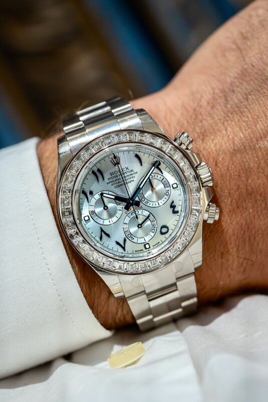 A Rolex Daytona in white metal with a pale satin dial, Eastern Arabic numerals and a diamond-set bezel, on its bracelet under a white cuff