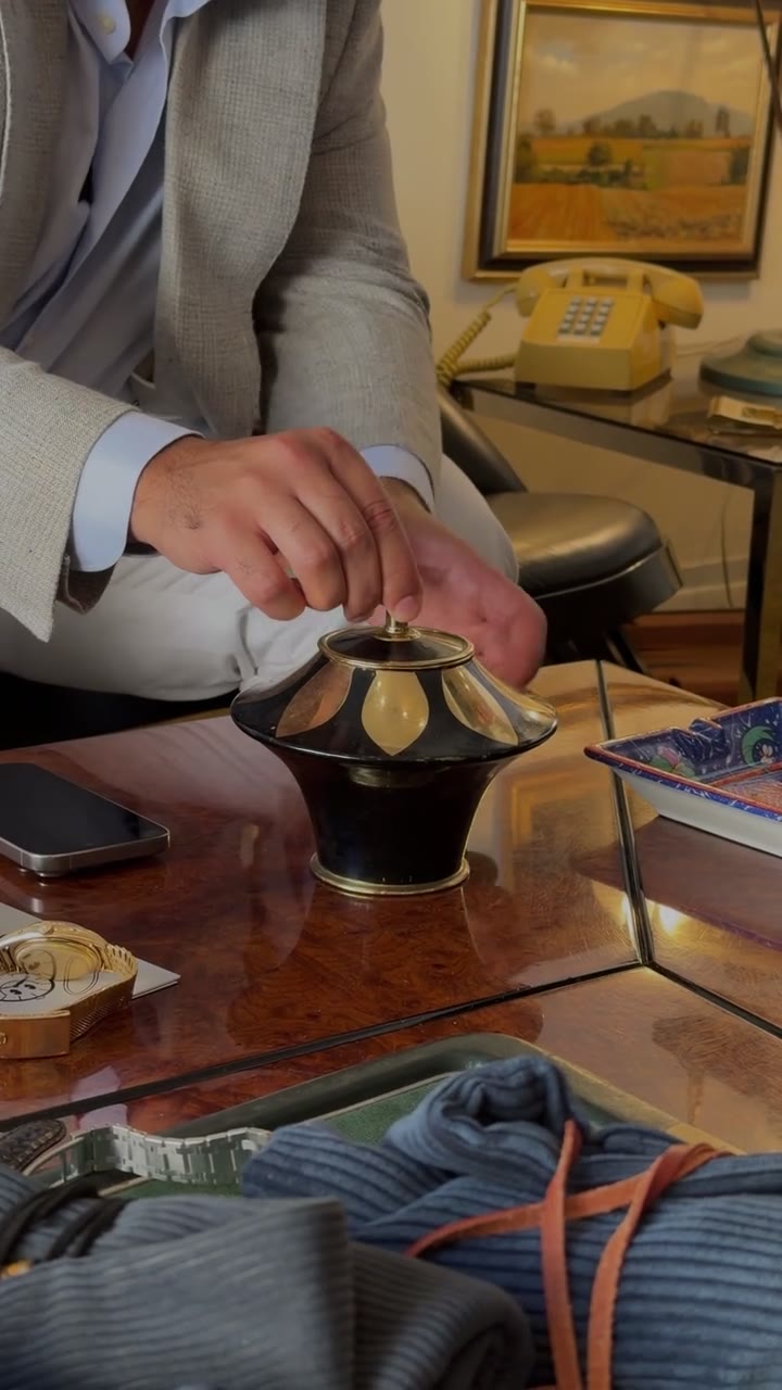 Video: a black-and-gold cigarette dispenser opened on a coffee table, cigarettes fanning out under the lifted lid, a yellow telephone and framed pictures behind