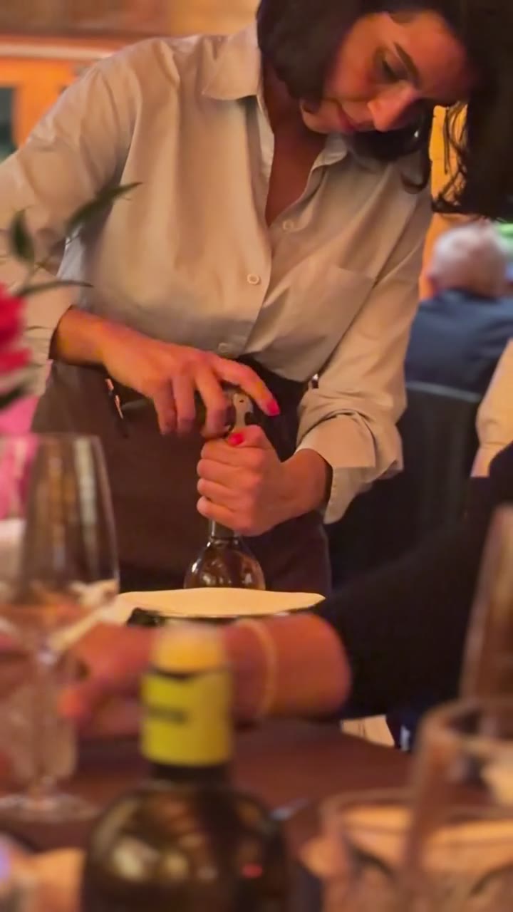 Video: a server uses a corkscrew to open a bottle of wine beside an ice bucket at the dinner table