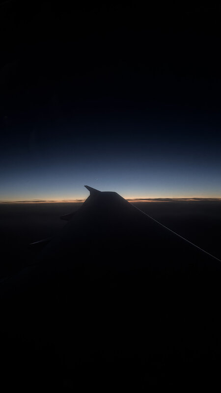 Airplane wing silhouette against sunset — flying into Geneva