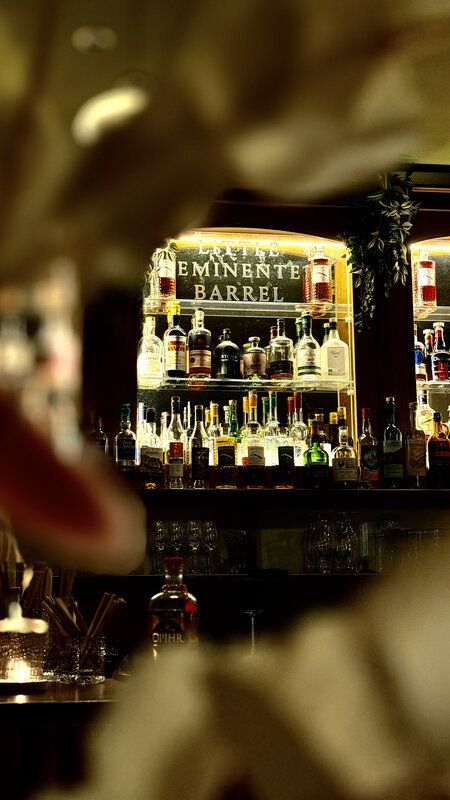 Backlit Eminente Barrel bar wall with rum bottles — soft foreground bokeh of a wine glass
