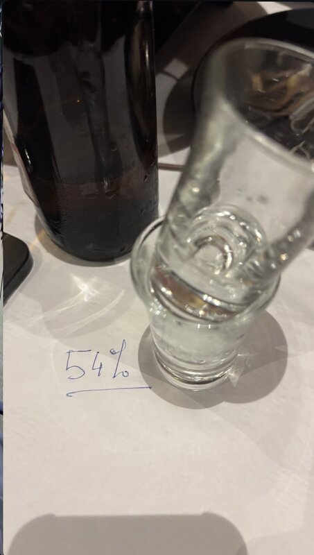 Tasting glass beside a dark bottle on a paper marked '54%' — cask sample at a Geneva tasting
