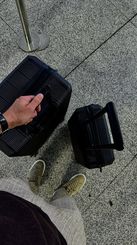 Two black suitcases in the terminal queue, one lying flat, seen from above with his trainers in frame