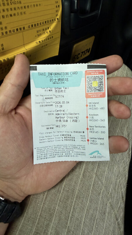 A hand holding a printed Hong Kong taxi information card with route and fare details