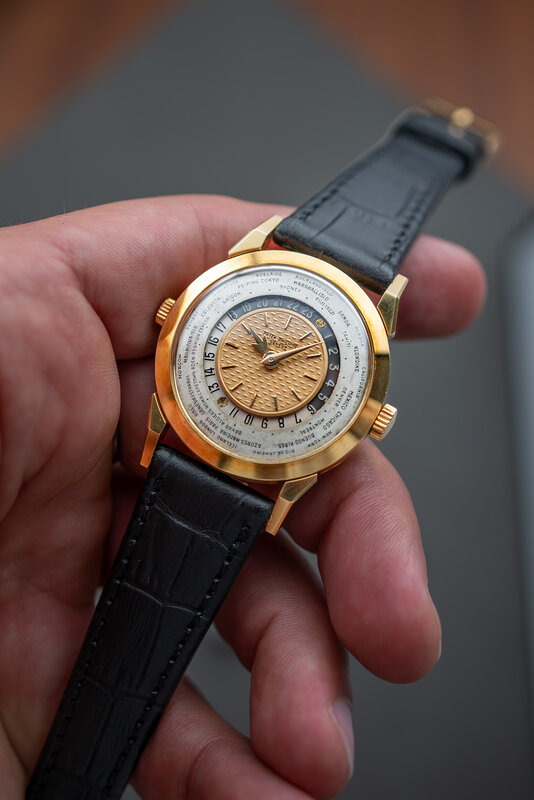 The yellow-gold Patek Philippe 2523 held in hand, salmon guilloche centre and silvered city ring facing the camera, black alligator strap across the fingers