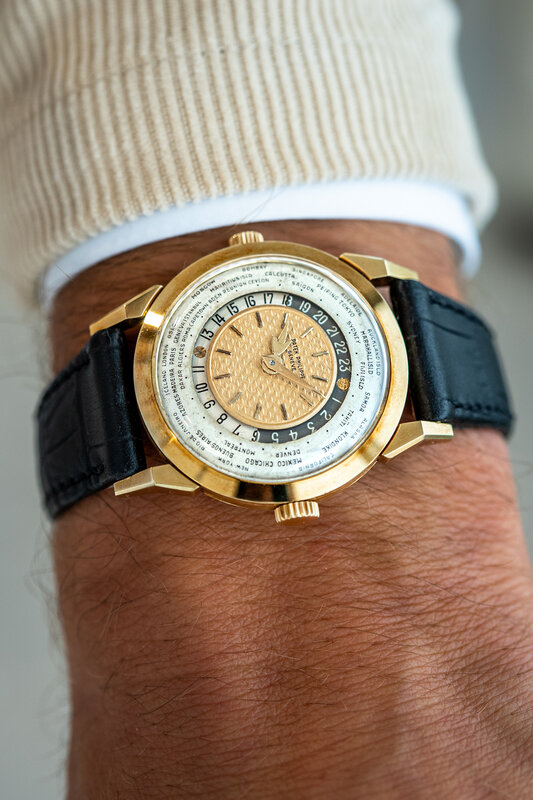 The Patek Philippe 2523 worn on the wrist below a ribbed cream sweater cuff, world-time dial catching the daylight