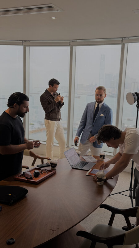 The shoot in progress in an office above Victoria Harbour, a round table, a laptop, a lighting stand and four people working, floor-to-ceiling windows onto the water