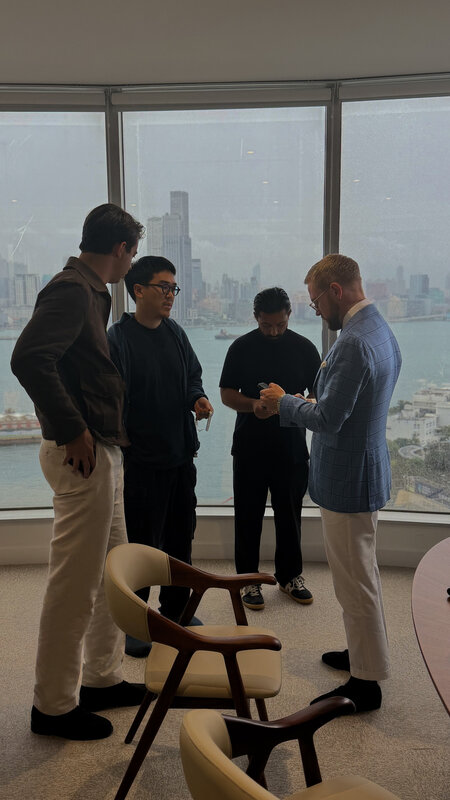 Four men standing and talking by the office window, the Kowloon skyline hazy across the water