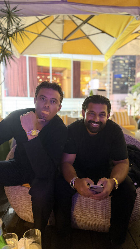 Rutger and Ramon on rattan chairs under a yellow parasol at night, one pulling a face at the camera