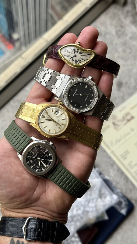 Four watches held in one hand, a curved Cartier on burgundy leather, a diamond-bezel Audemars Piguet on steel, a gold Rolex on a gold bracelet and a steel Patek Philippe on green rubber