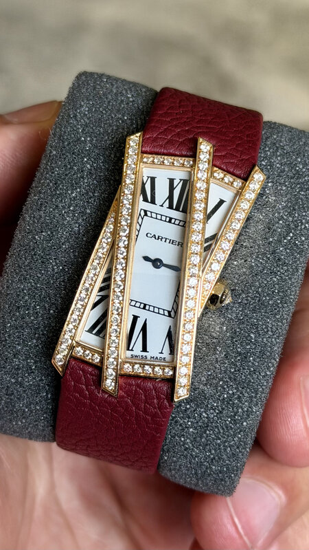 A gem-set Cartier with an elongated white Roman-numeral dial and three diamond bars across it, on a burgundy leather strap, held in a hand