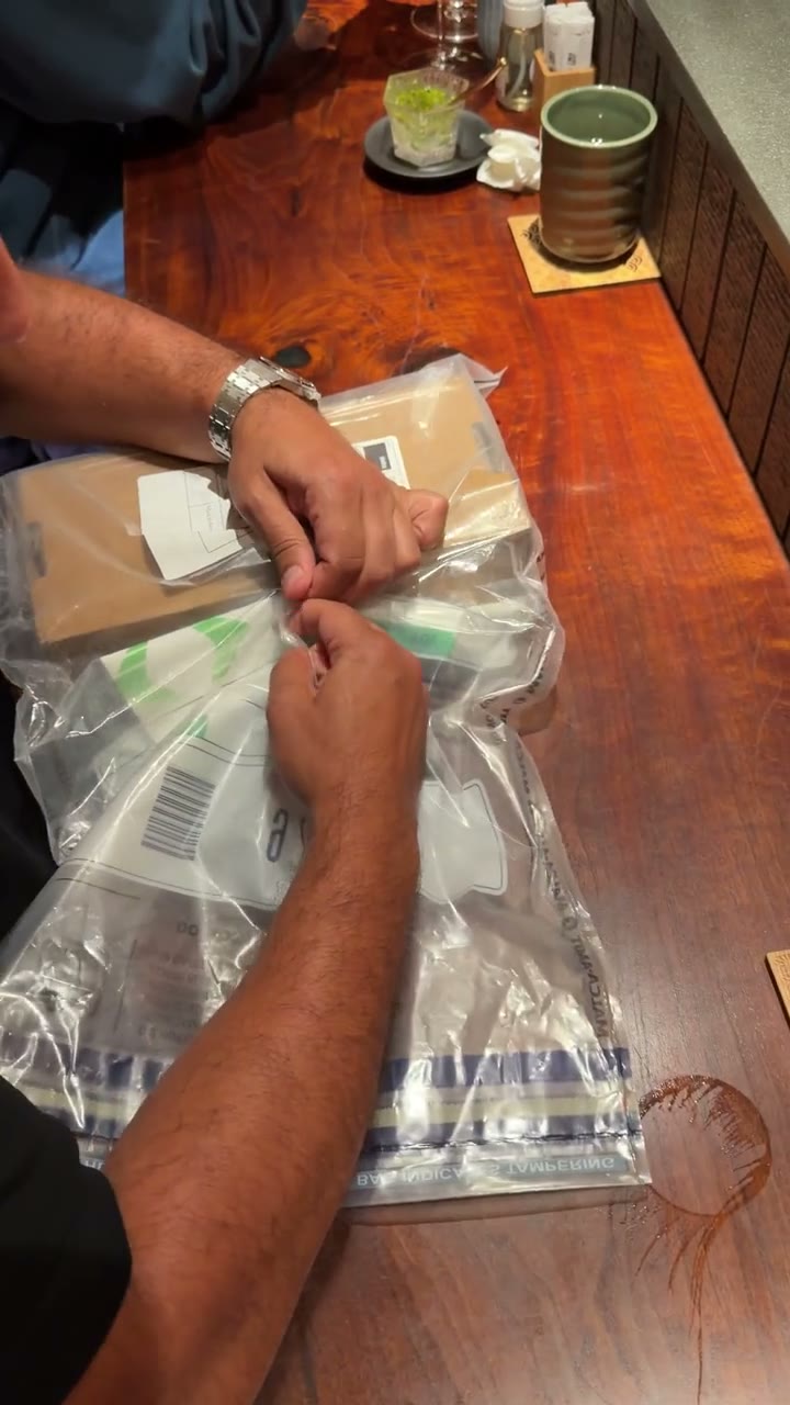 Video: hands unwrapping a padded parcel at a wooden table, a watch box beside it
