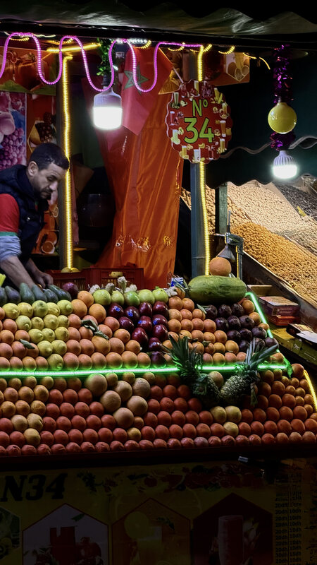 Fruit stall in Jemaa el-Fna square at night — oranges, pineapple, neon lights