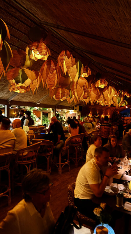 Wide view of the Kabana rooftop at night — orange-lit woven lantern ceiling, full bar, guests at tables